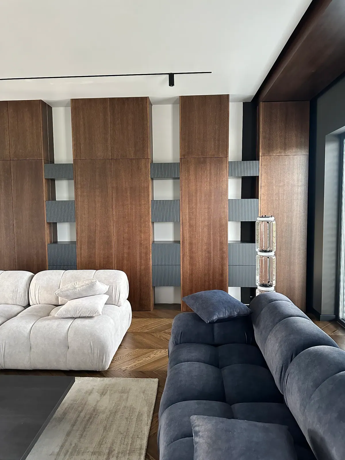 Wohnraum mit deckenhoher Schrankwand in Nussbaumfurnier und Nischen mit graphitfarbenen, geriffelten Schubladen